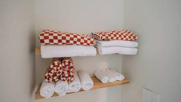 Une chambre d’hôtel avec une étagère en bois où sont soigneusement pliées des serviettes aux motifs écossais rouges et blancs, ainsi que des serviettes blanches unies.