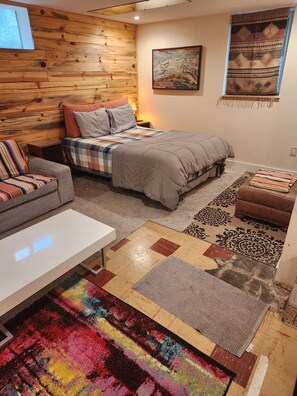 A cozy bedroom with a wooden headboard, a bed with a beige comforter, a colorful striped sofa, and a white bedside table.