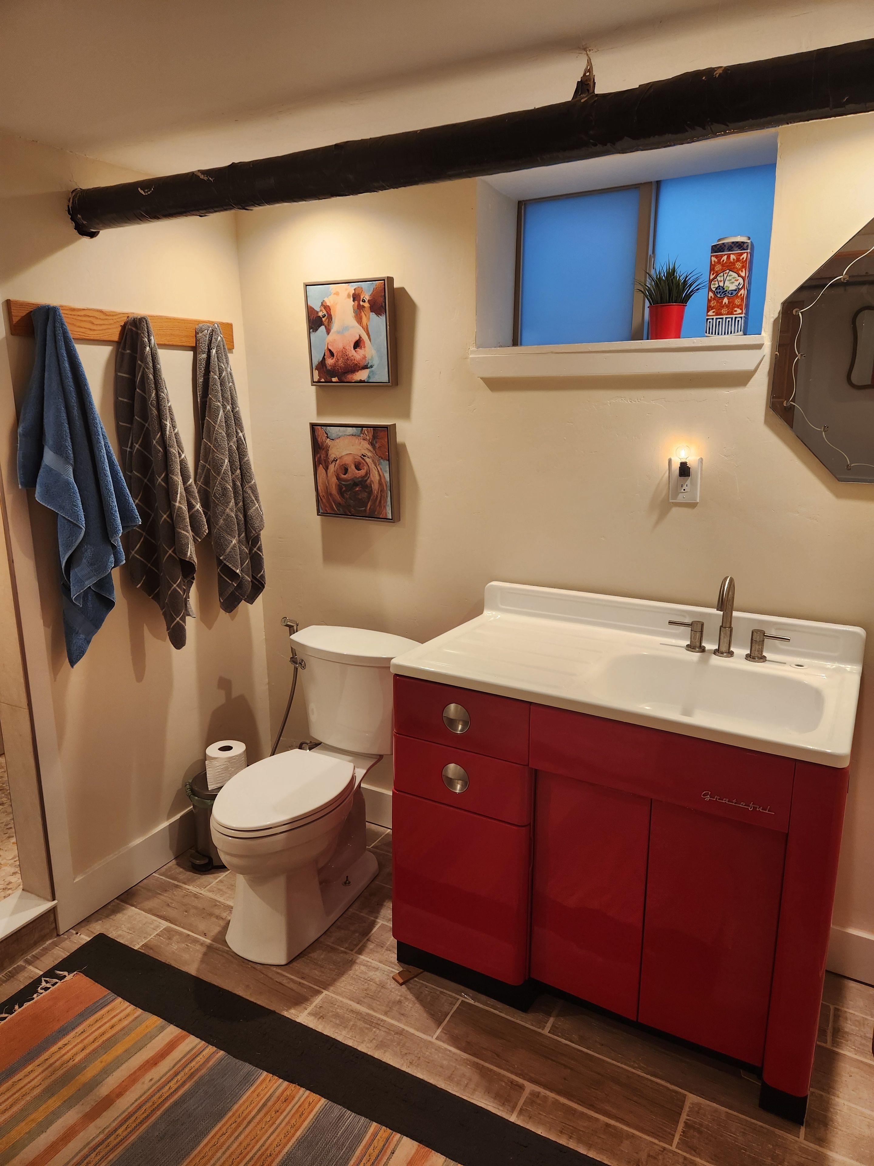 Ein Badezimmer mit einer weißen Toilette, einem roten Waschtisch und einem Fenster über dem Waschbecken.