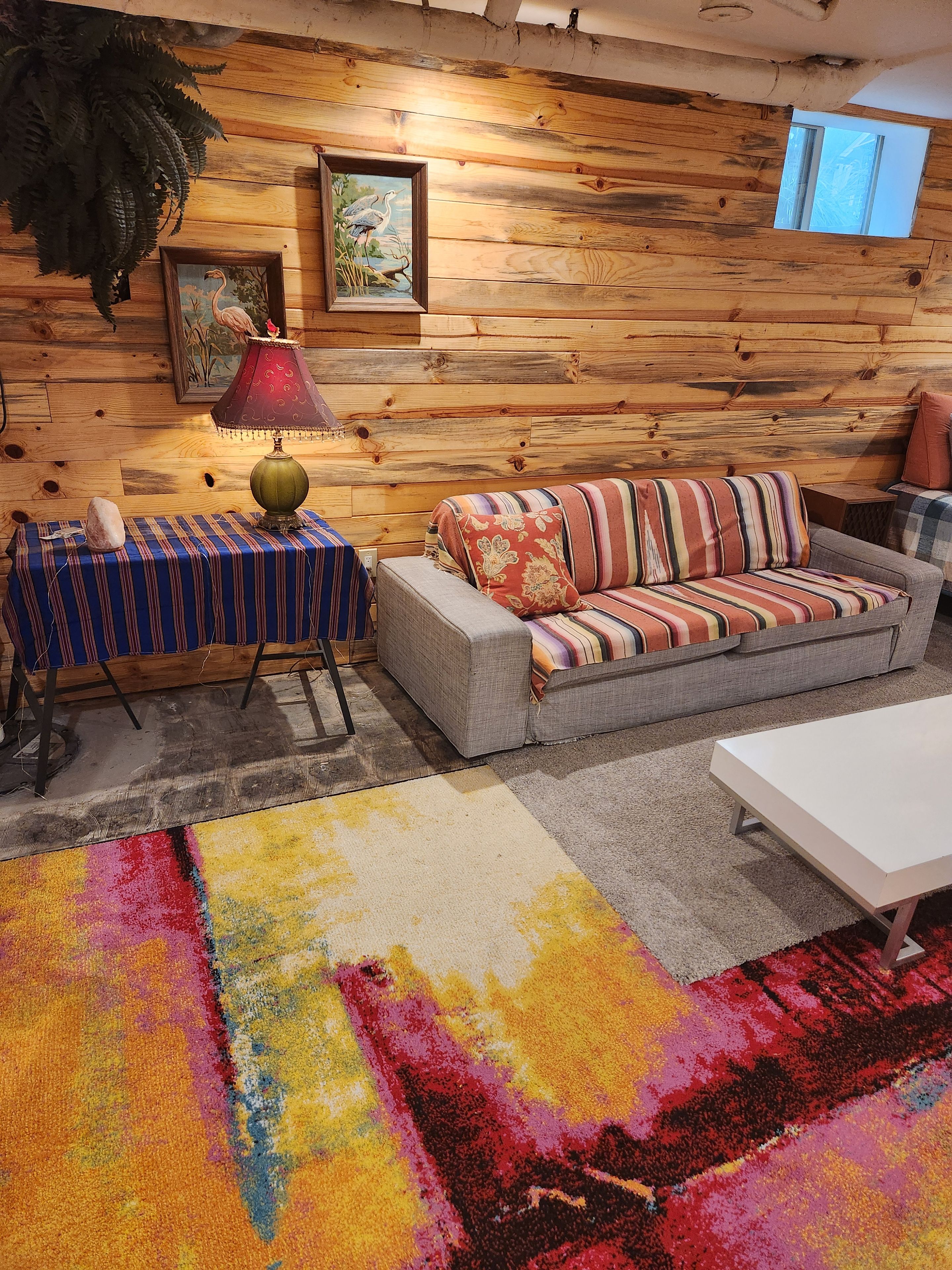Ein gemütliches Wohnzimmer mit einer Holzwand, einem Sofa, einem Tisch und einem farbenfrohen Teppich.