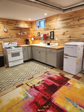 A kitchen with wooden walls, a gas stove, a refrigerator, a sink, and a patterned rug.
