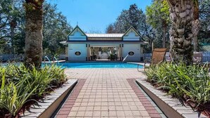 Un espace piscine doté d’un coin salon abrité, entouré de palmiers et de plantes.