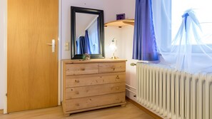 Une pièce avec une commode en bois, un miroir, un radiateur et une fenêtre ornée de rideaux bleus.
