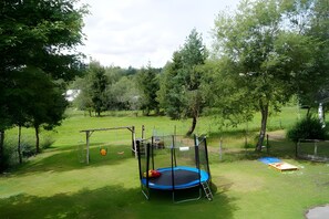 Un espacio al aire libre con césped, un trampolín, un columpio y una pequeña estructura de juegos.