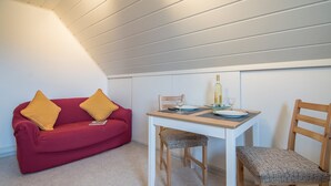 A compact room with a red sofa, two wooden chairs, a small table, and a bottle of wine.