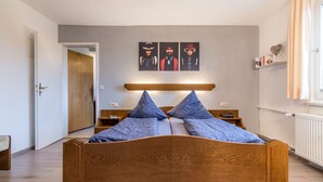 A bedroom with a wooden bed, a headboard, a nightstand, a bedside table, and a wall-mounted shelf with books.