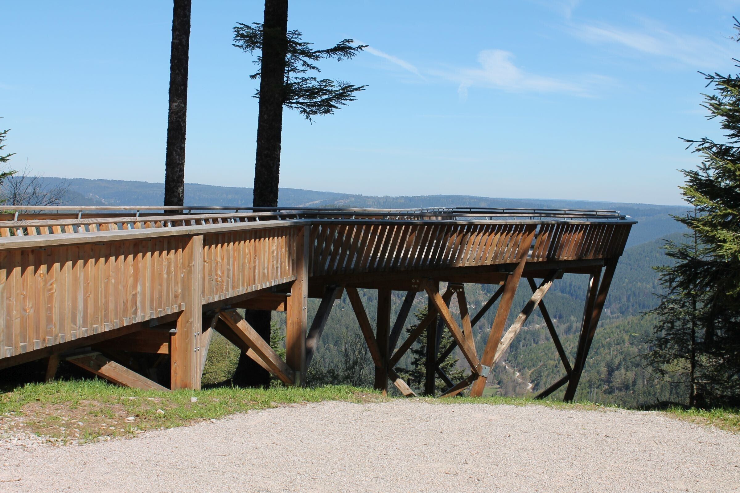 A wooden observation deck with a gravel path leading to it, overlooking a forested valley.