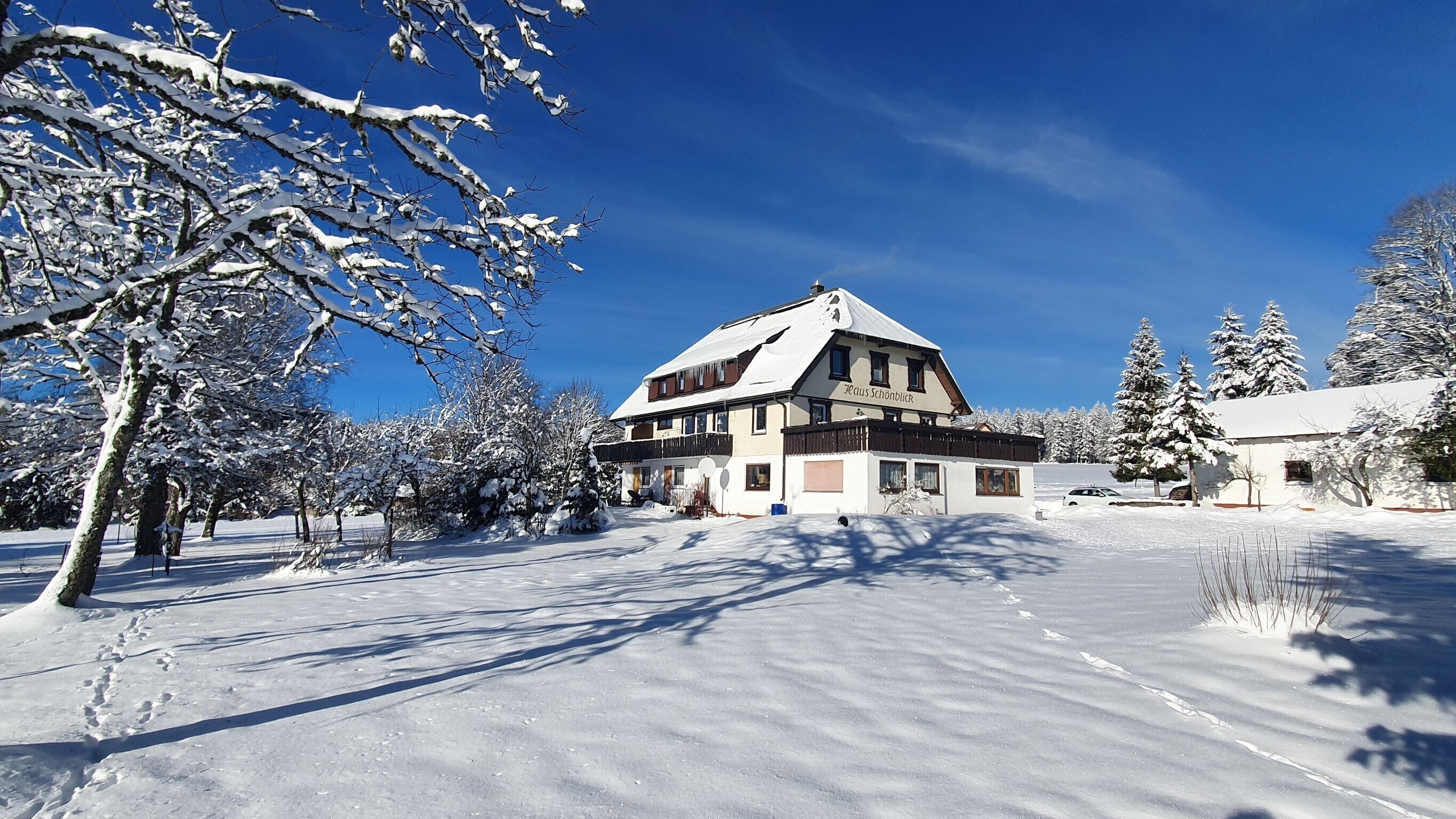 A two-story building with a sloped roof, surrounded by snow-covered trees and a clear blue sky.
