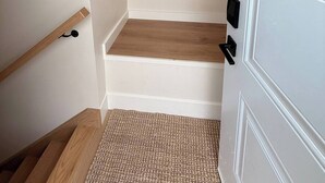 A narrow hallway with a wooden floor, a white door with a black handle, and a white wall with a light switch.