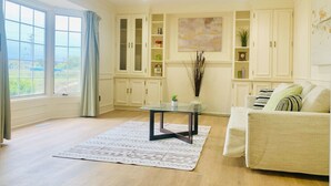 Amplia sala de estar con un ventanal, una mesa de centro de vidrio, un sofá color beige y armarios empotrados blancos.