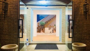 Entrada con puerta de vidrio a una propiedad con muro de ladrillo, escalera de madera y un pequeño espacio de estar al aire libre visible a través de la puerta.