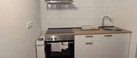 A compact kitchen with a built-in oven, a stainless steel range hood, a sink, and a wooden countertop.