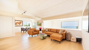A spacious living room with a large window, a sofa, a coffee table, and a dining area. - NEW!!! Ocean View Malibu Modern Home w/ Mini Golf & Spa (Malibu)