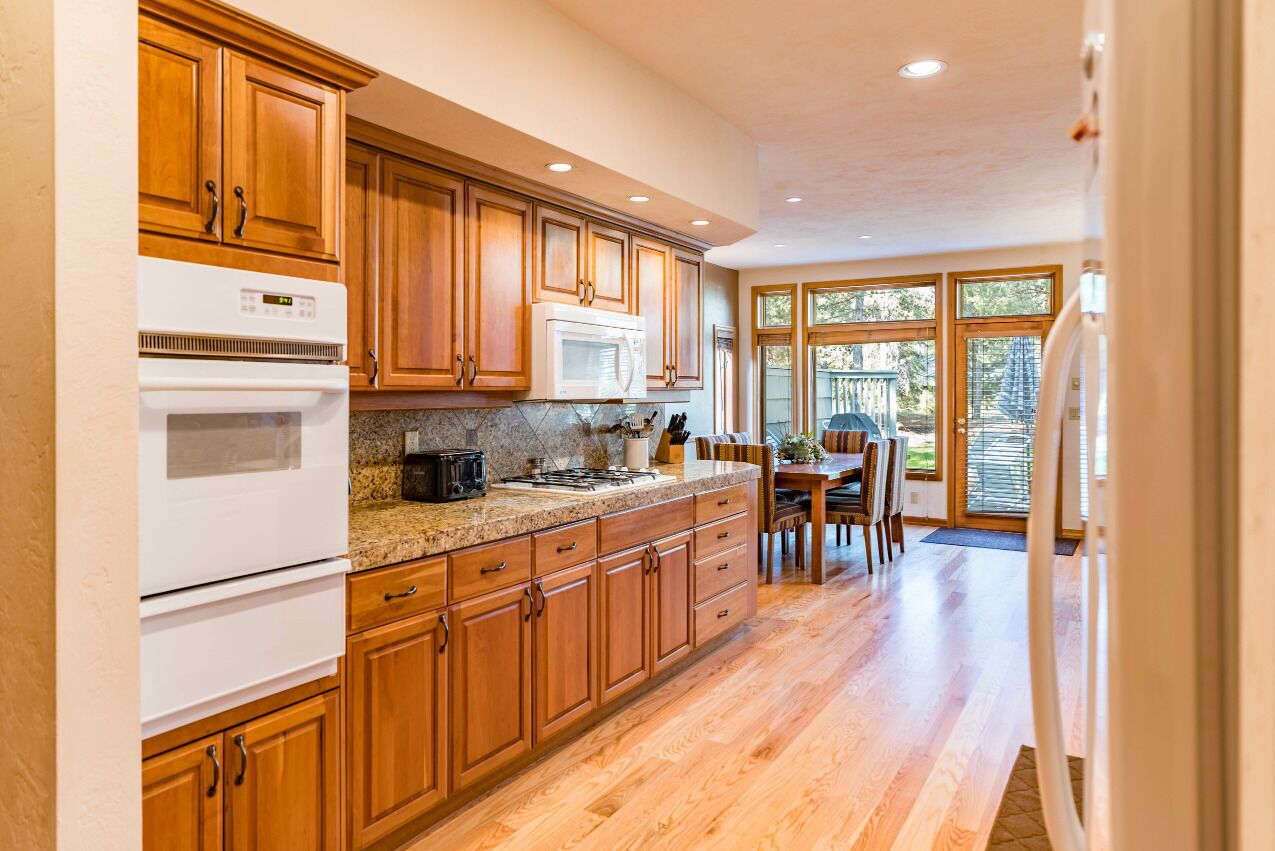 A kitchen with wooden cabinets, a white stove, a microwave, and a dining area with a table and chairs.