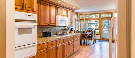 A kitchen with wooden cabinets, a white stove, a microwave, and a dining area with a table and chairs.