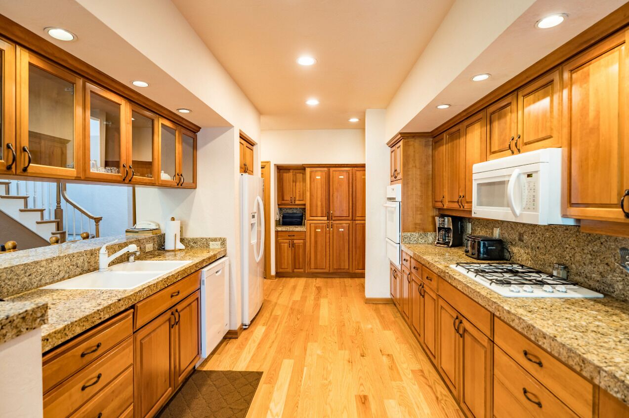 A kitchen with wooden cabinets, granite countertops, a white refrigerator, a microwave, and a gas stove.