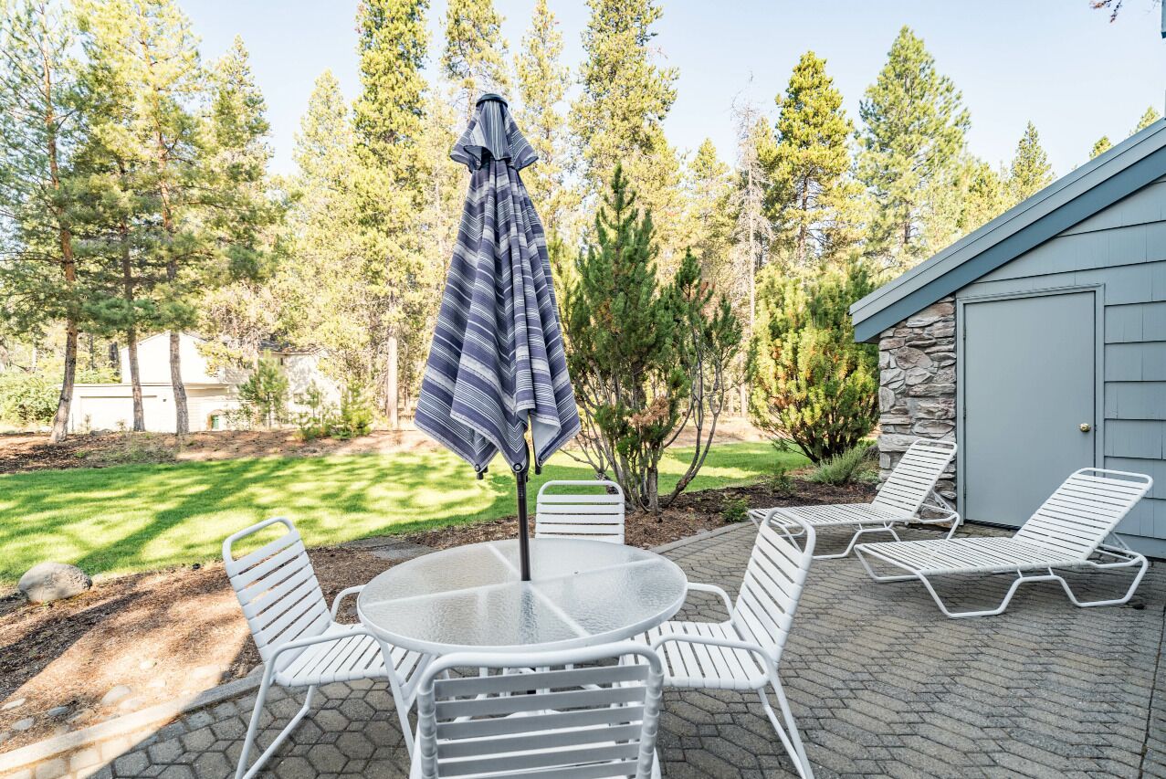 A patio with a round table and four chairs, an umbrella, and two lounge chairs.