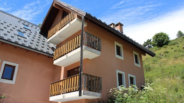 A two-story building with balconies, a sloped roof, and a hillside background. - Les Faons - ROUBION - Gîte (ROUBION)