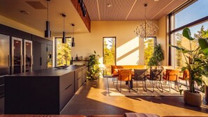 Une cuisine moderne dotée d’un îlot central, d’un coin repas avec une table et des chaises en bois, et de grandes fenêtres qui laissent entrer la lumière naturelle.