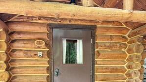 Une cabane en rondins avec une porte marron, deux bancs en bois et un paillasson.