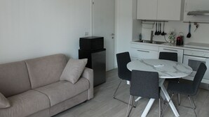 A compact living space with a sofa, a dining table with chairs, a kitchen area with cabinets and utensils, and a compact refrigerator. - Central Stay, Cozy Way (Milano)