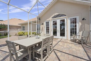 Een terras met een tafel en stoelen, een overdekte zithoek, en een huis met een pannendak en een witte gevel.