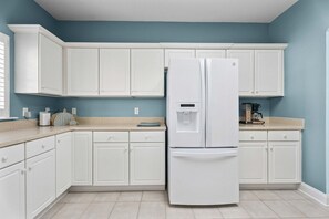 Une cuisine avec des armoires blanches, un réfrigérateur blanc et un plan de travail beige.