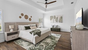 Une chambre à coucher comprenant un lit, des tables de chevet, un ventilateur de plafond, des œuvres d’art et un téléviseur.