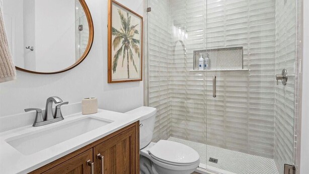 Une salle de bain avec un lavabo blanc, des toilettes, une douche avec une porte en verre et un tableau encadré au mur.