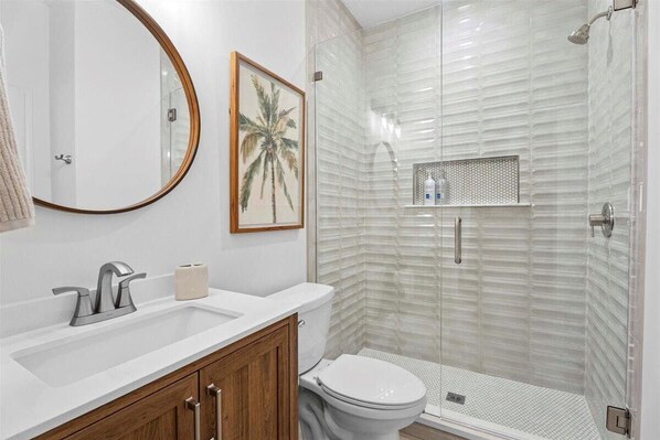 A bathroom with a white sink, a toilet, a shower with a glass door, and a framed picture on the wall. - Stunning 3 BR 3 BA luxury  beach home in St. Augustine, FL (Saint Augustine)