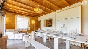 A dining area with a long table set for a meal, wooden ceiling beams, and a white sofa in the background.