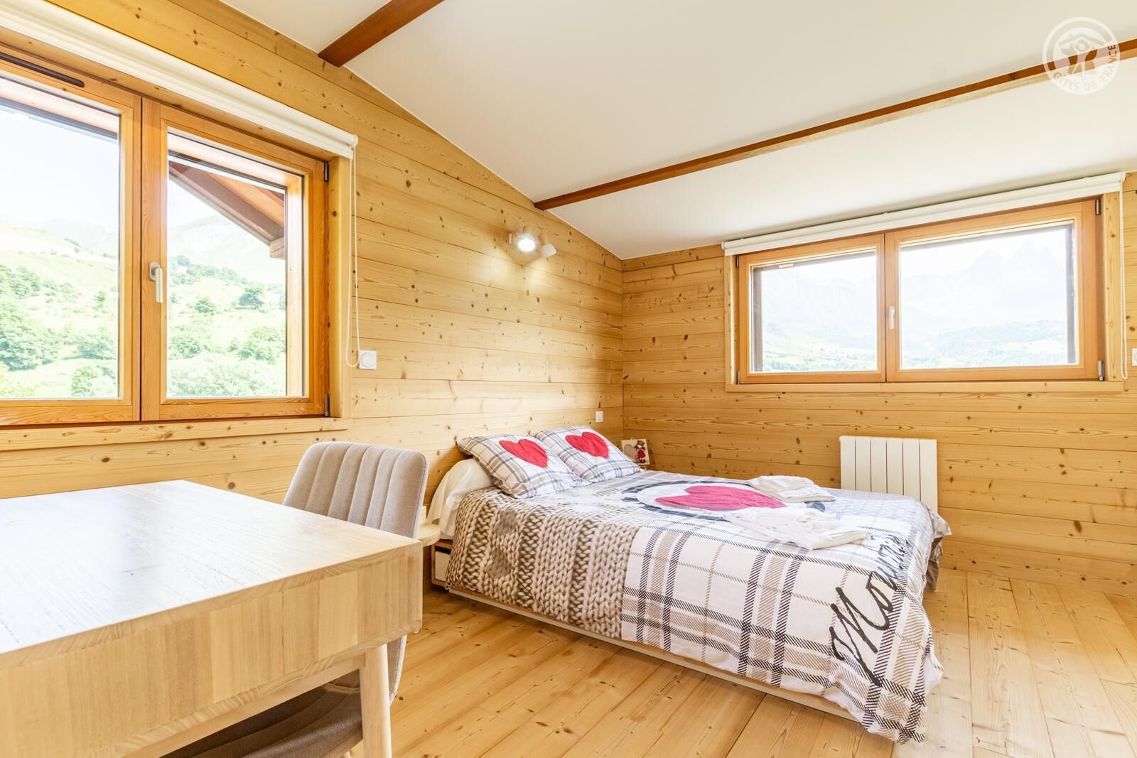 Ein Schlafzimmer einer Holzhütte mit einem Bett, einem Schreibtisch und zwei Fenstern.