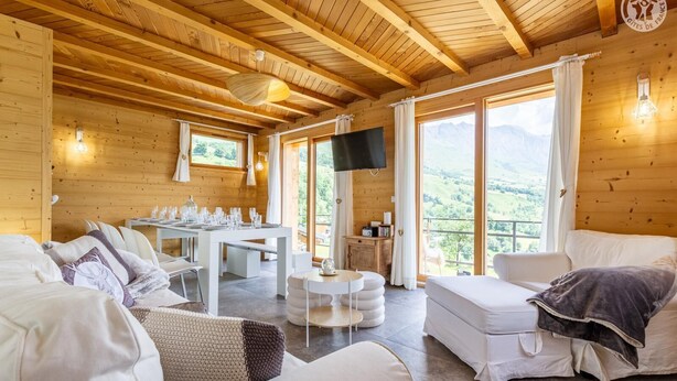 A cozy wooden cabin with a dining area, a TV, and a balcony with a mountain view.