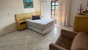 A bedroom with a bed, a wooden nightstand, a small table, a sofa, a painting on the wall, and a window with curtains.
