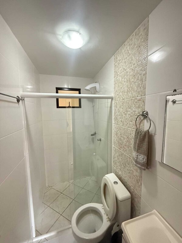 Un baño pequeño con ducha de vidrio, inodoro y perchero para toallas.