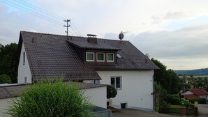 A two-story house with a sloped roof, a satellite dish, and a small garden area with bushes.
