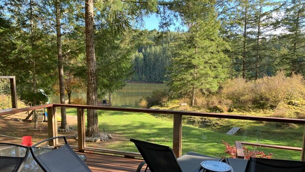 A deck with outdoor seating and a view of a lake surrounded by trees.