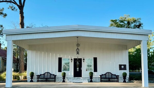 A white pavilion with a black door and two windows, benches, and a plaque on the wall. - NSW Inn (Sylvester)