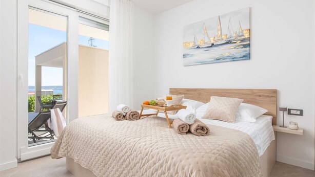A bedroom with a bed, a bedside table, a painting, and a view of the outdoors. - Villa Vista Vinea – Private heated pool villa close to Split and Trogir (Kaštel Novi)