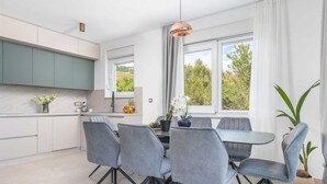 A modern kitchen with grey cabinets, a dining table with four grey chairs, and a large window with curtains. - Villa Vista Vinea – Private heated pool villa close to Split and Trogir (Kaštel Novi)