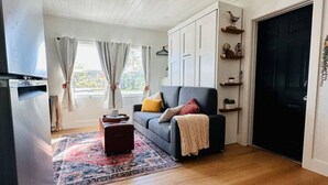 A modern living room with a sofa, a coffee table, and a rug. There is a black door and a window with curtains. - Naples Serene Studio (Naples)
