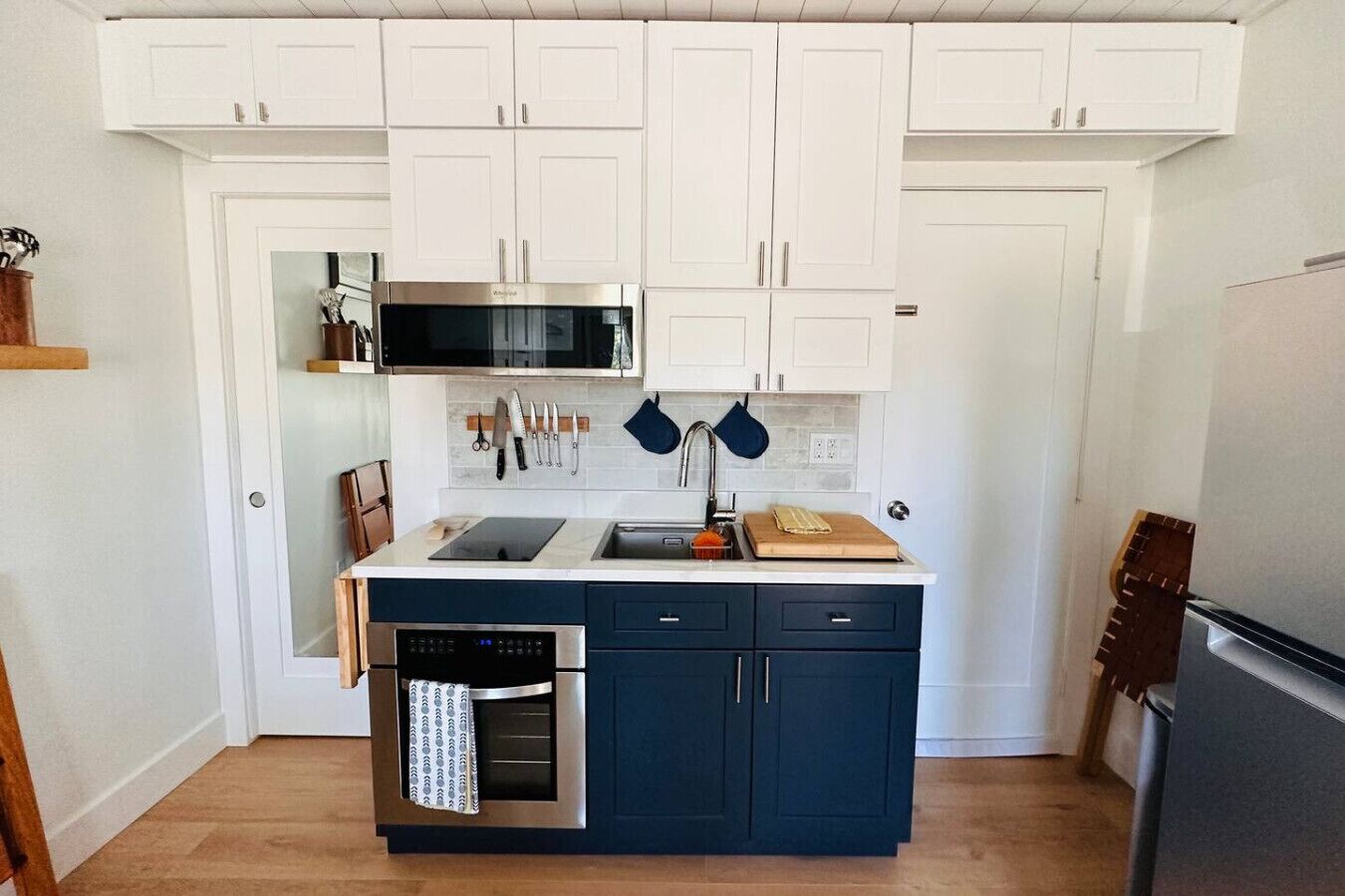 A compact kitchen with white upper cabinets, a black microwave, a built-in oven, and a blue lower cabinet.