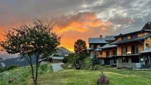 Un chalet rustique à la façade en pierre, doté de plusieurs balcons et offrant une vue sur une chaîne de montagnes.