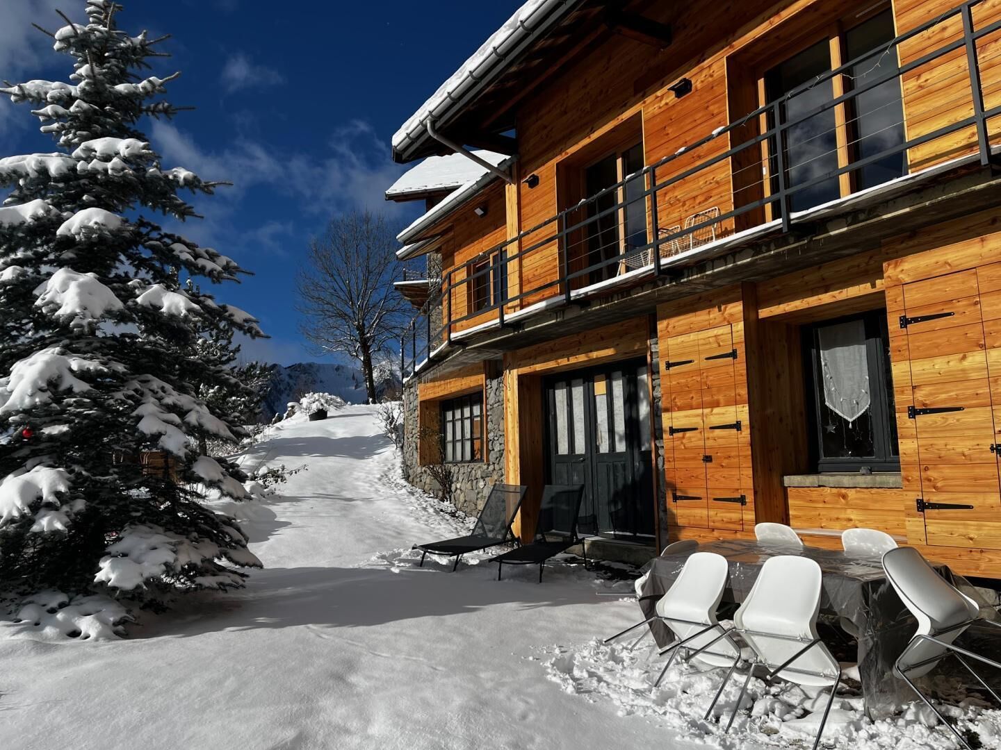 Una cabaña de madera con balcón, un área de estar exterior cubierta y un paisaje cubierto de nieve.
