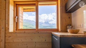 Une cuisine rustique aménagée dans une cabane en bois, avec une grande fenêtre donnant sur les montagnes.