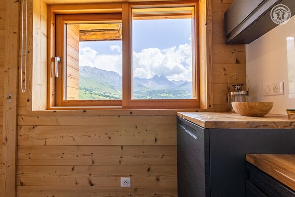 Une cuisine rustique aménagée dans une cabane en bois, avec une grande fenêtre donnant sur les montagnes.
