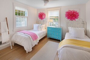Une chambre avec deux lits, une fenêtre avec des stores, une commode bleue et un radiateur blanc.