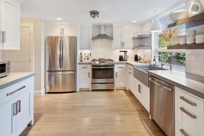 A modern kitchen with stainless steel appliances, white cabinetry, and a wooden floor. - Modern Saltbox in Edgartown Village (Edgartown)