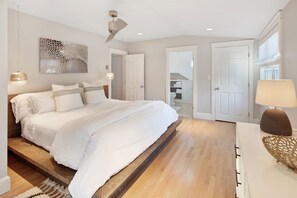 Ein modernes Schlafzimmer mit einem großen Bett, Holzboden, weißen Wänden und einem Deckenventilator.