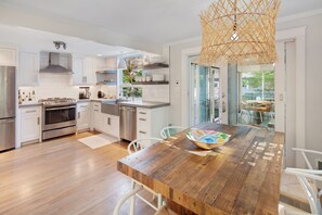 A modern kitchen with white cabinetry, stainless steel appliances, and a wooden dining table with a woven light fixture.